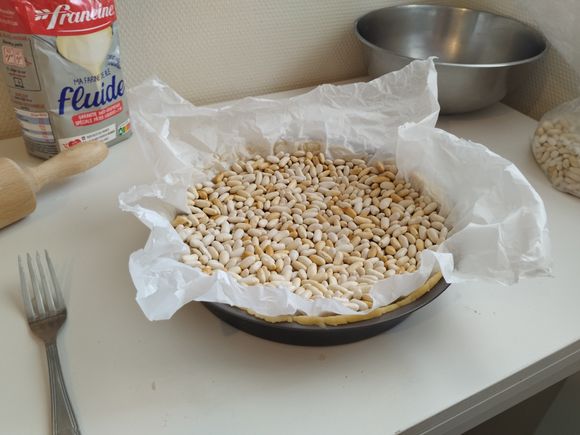Place some weight inside the pie crust, typically some dried beans.
Bake the crust for 20 minutes at 200 °C or until the rim of the pie crust is starting to get brown.
Empty the pie crust. You can now trim the excess dough before putting it back into the oven for another 20 minutes or until it's fully baked.
